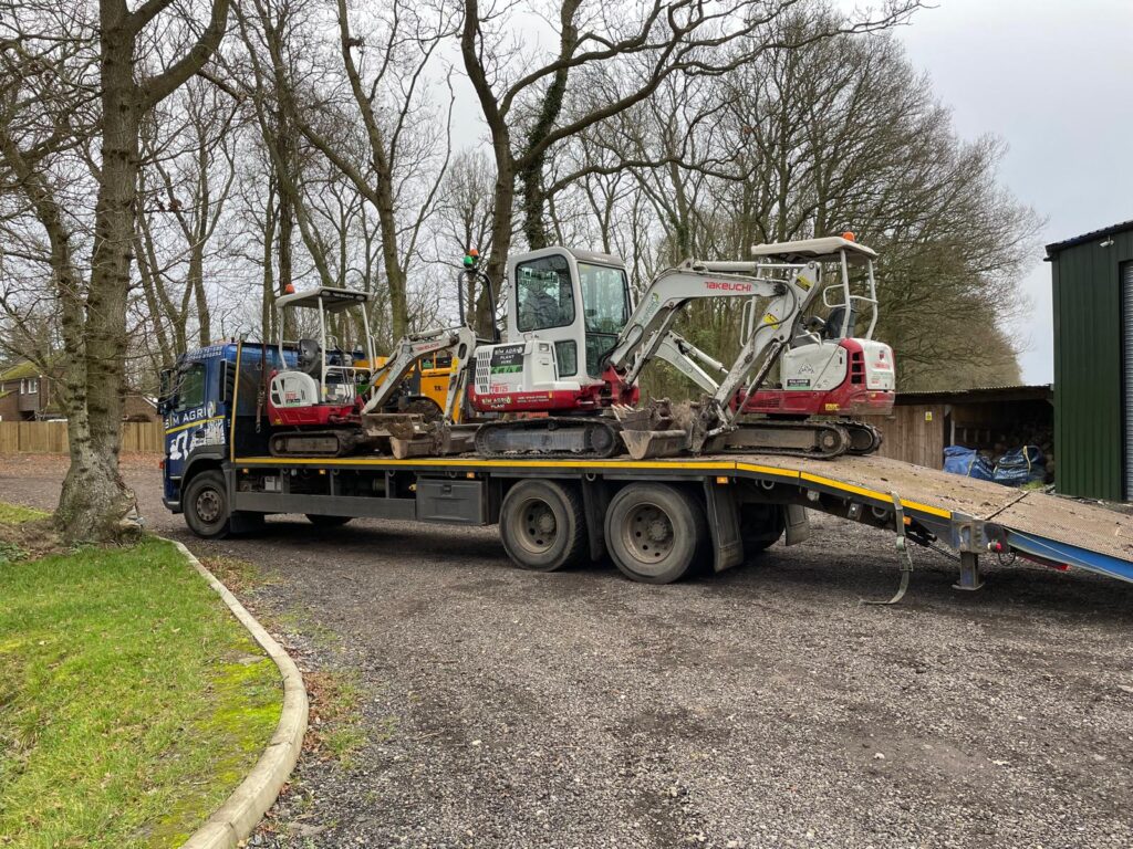 Two compact excavators being unloaded from a low-loader