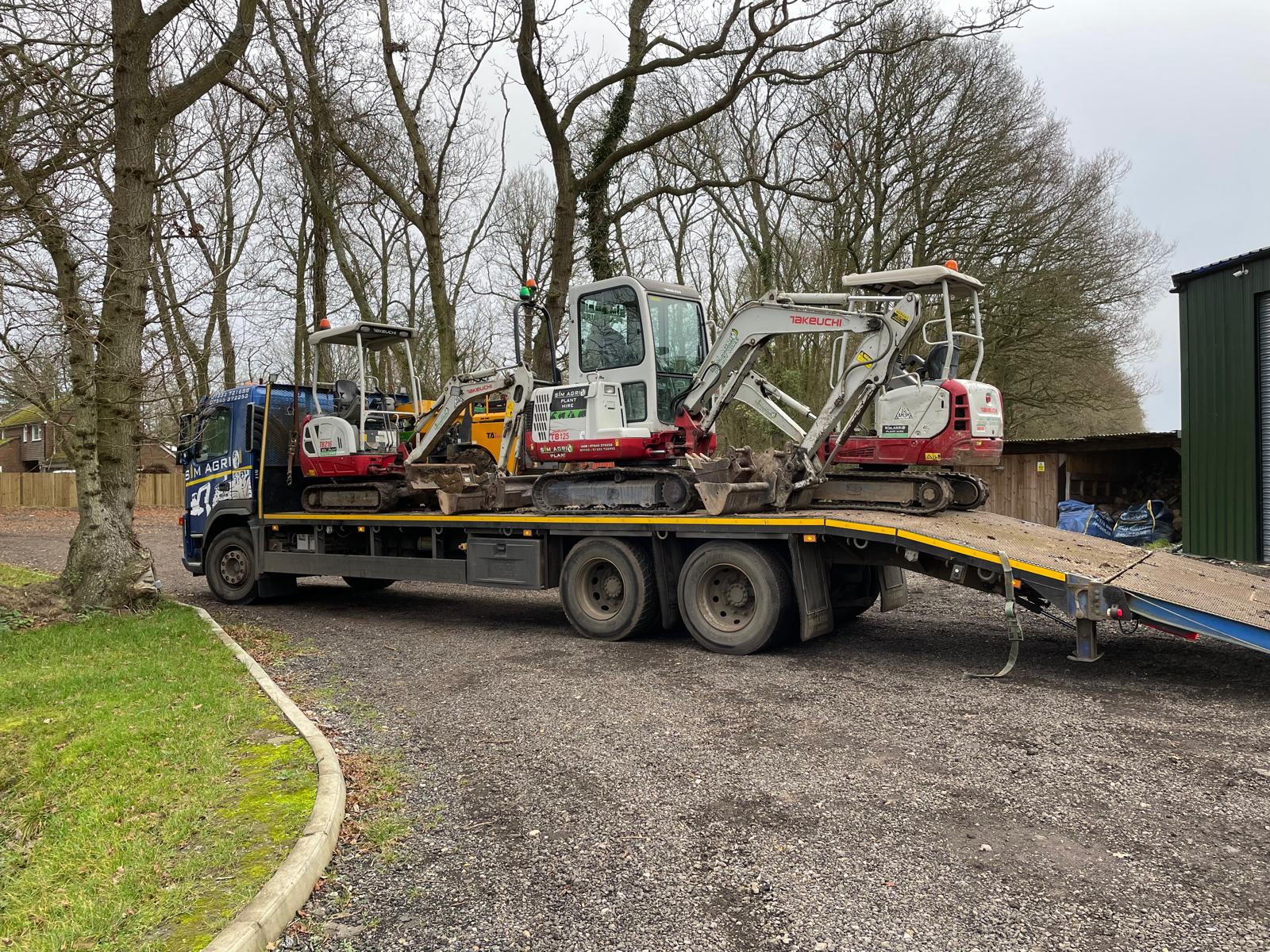Two compact excavators being unloaded from a low-loader
