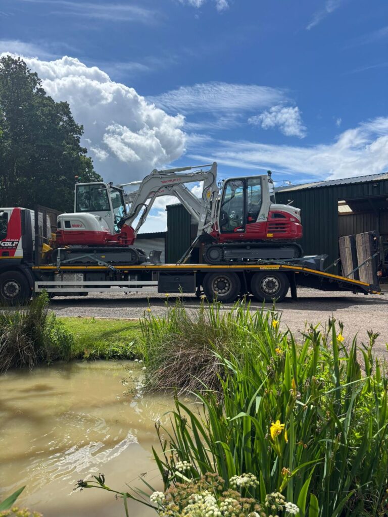 Compact excavator on a transport trailer viewed through foliage for the plant hire projects across the UK